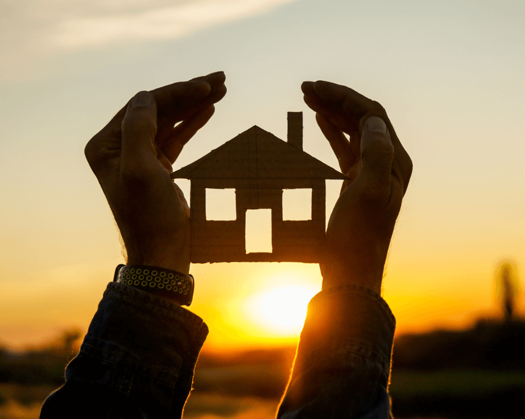 vente immobilière , maison tenue entre deux mains devant un coucher de soleil